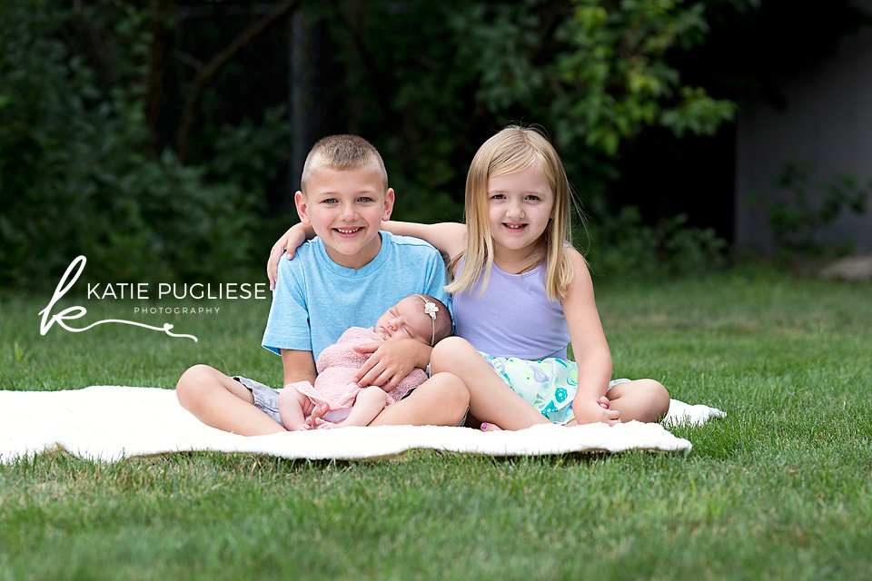 Older siblings posing outside with new baby sister